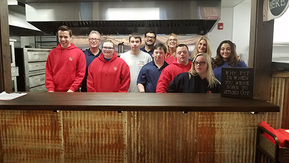 Employees and volunteers of No Limits Cafe, including owners Mark Cartier (second from left, rear) and Stephanie Cartier (fifth from right, rear) posed for a photo in the kitchen, which looks out over the dining area. Their daughter Katie is at right, front.